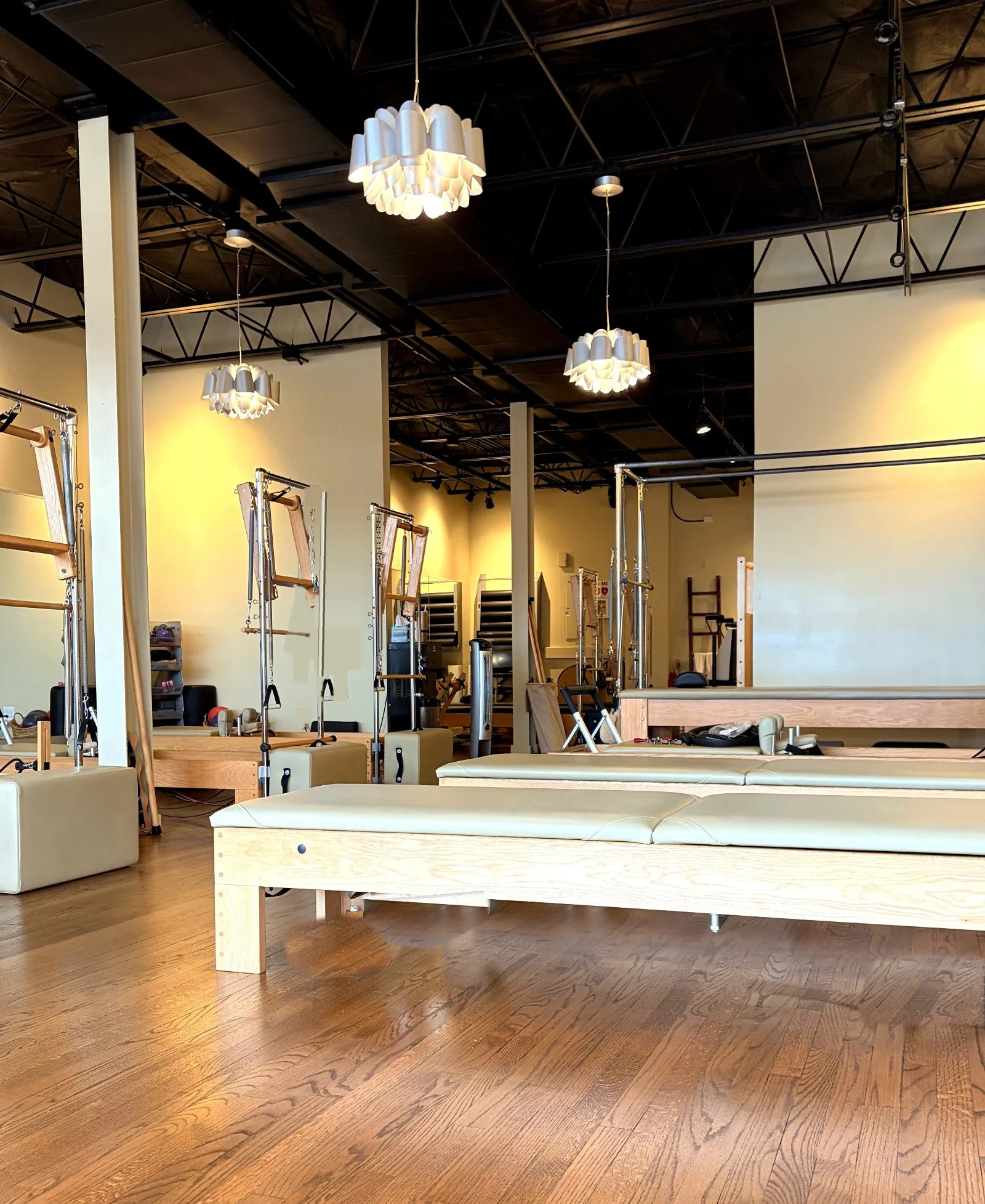 The Pilates Connection studio floor, lined with classical reformers beneath tall industrial ceilings and sculptural pendant lighting